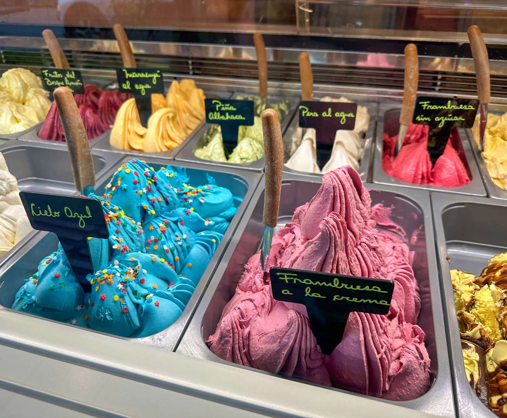 A display of colorful gelato sit in containers and labeled by their flavors.