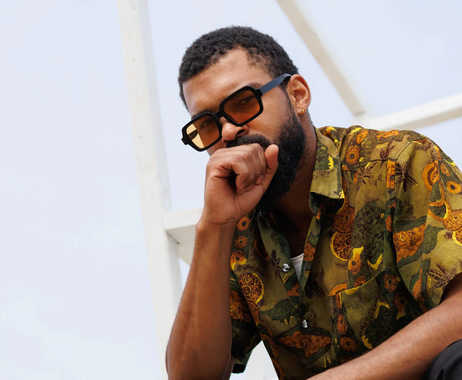 A man in black shades sits down, showing off his yellow and green shirt.