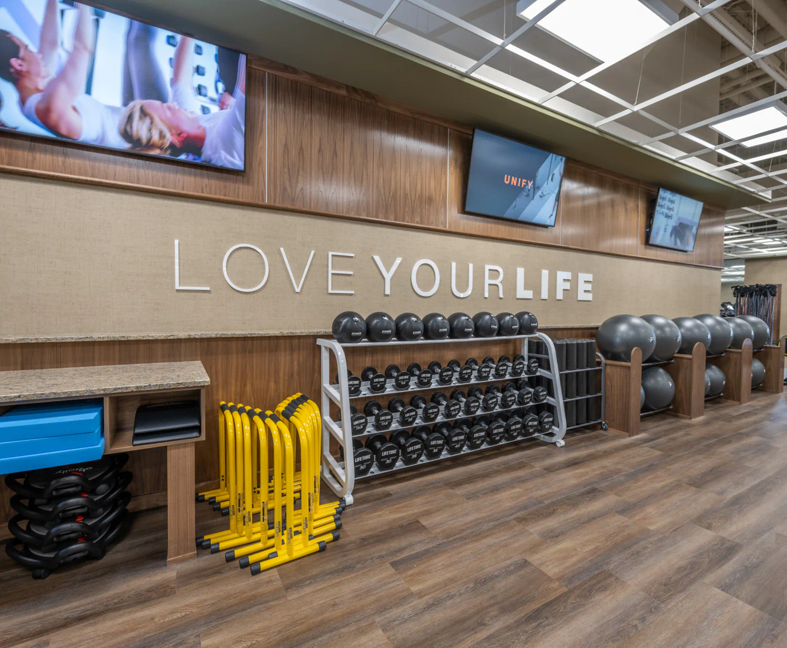 A series of medicine balls lay on a metal rack in a gym with wooden walls and floors.