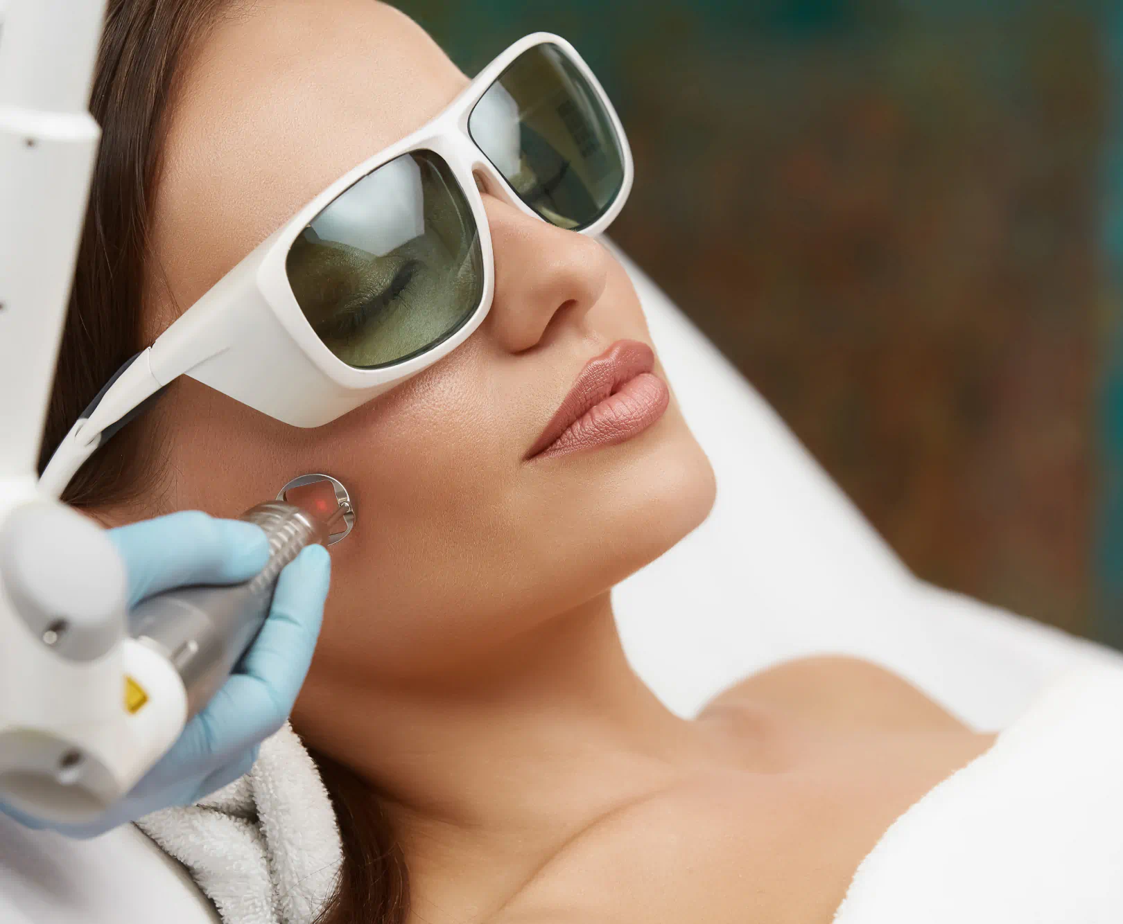 A girl lies with her eyes clothes as she get a laser treatment on skin.