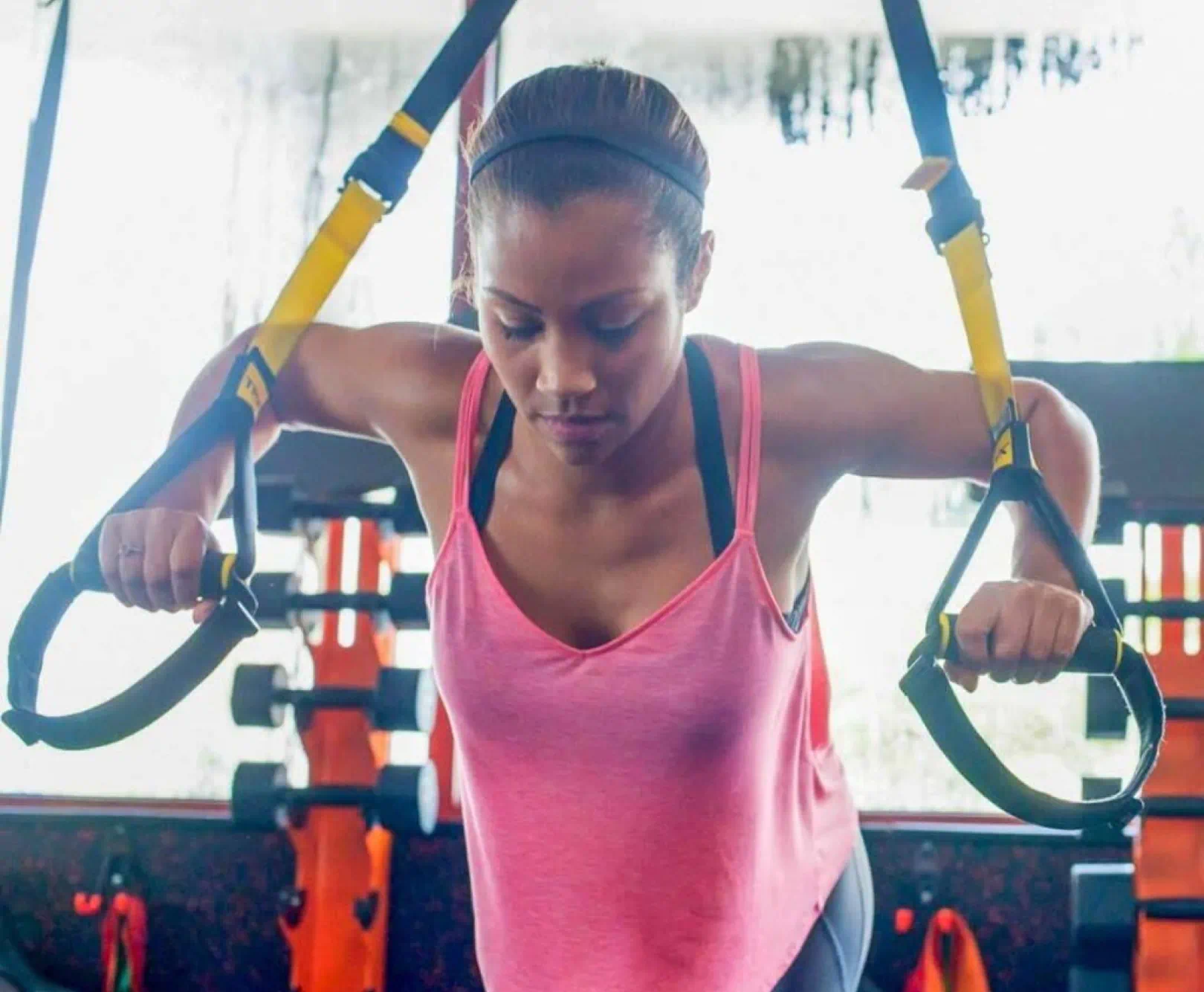 Woman performing TRX suspension training indoors using yellow and black straps.