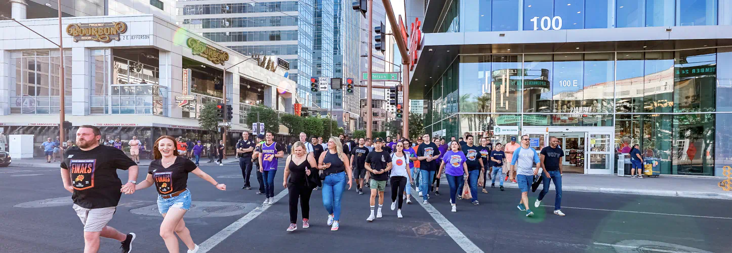 Lots of people in "Phoenix Suns" shirts cross at an intersection in CityScape.
