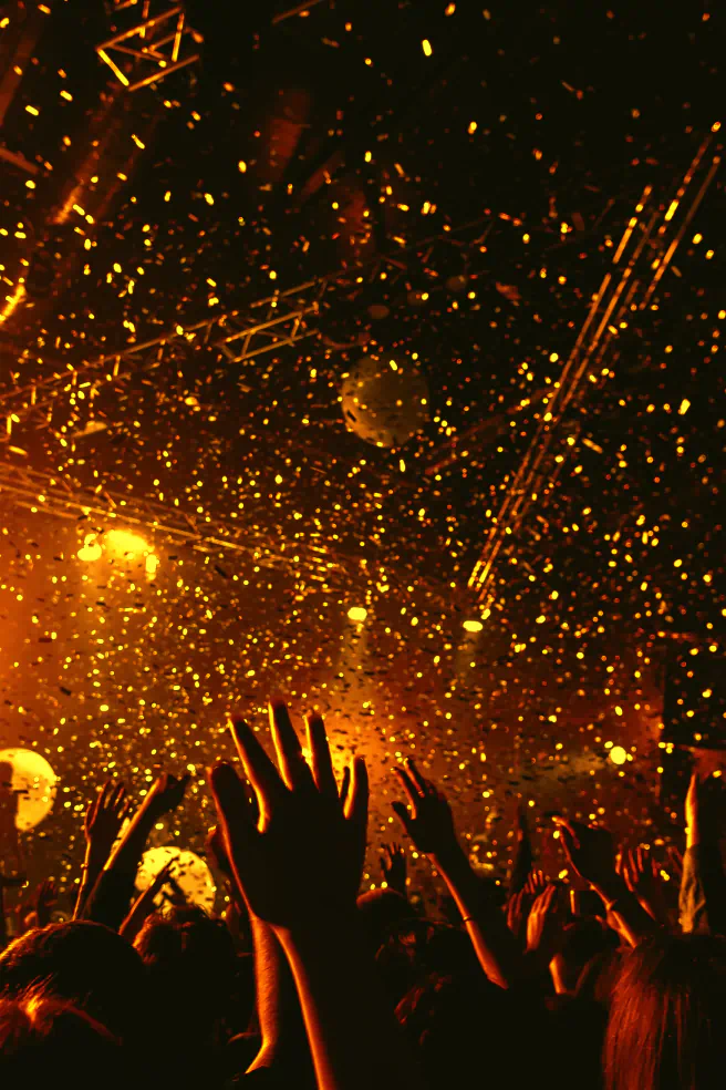 A crowd reaches into the air as confetti falls from above.