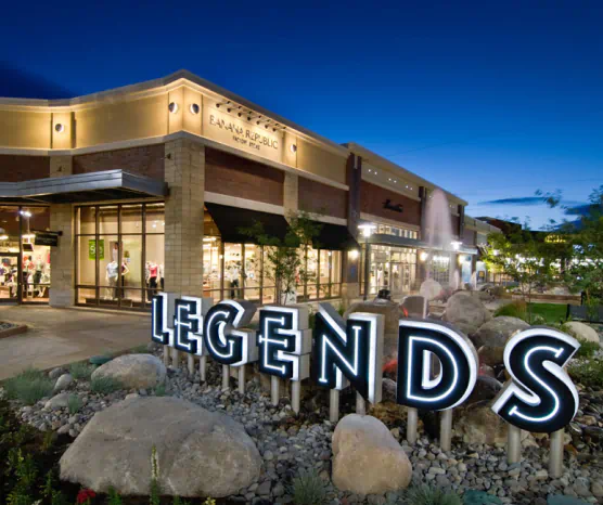 Exterior of The Outlets at Legends. Letters displaying "Legends" sit in front of a fountain with storefronts in the background.