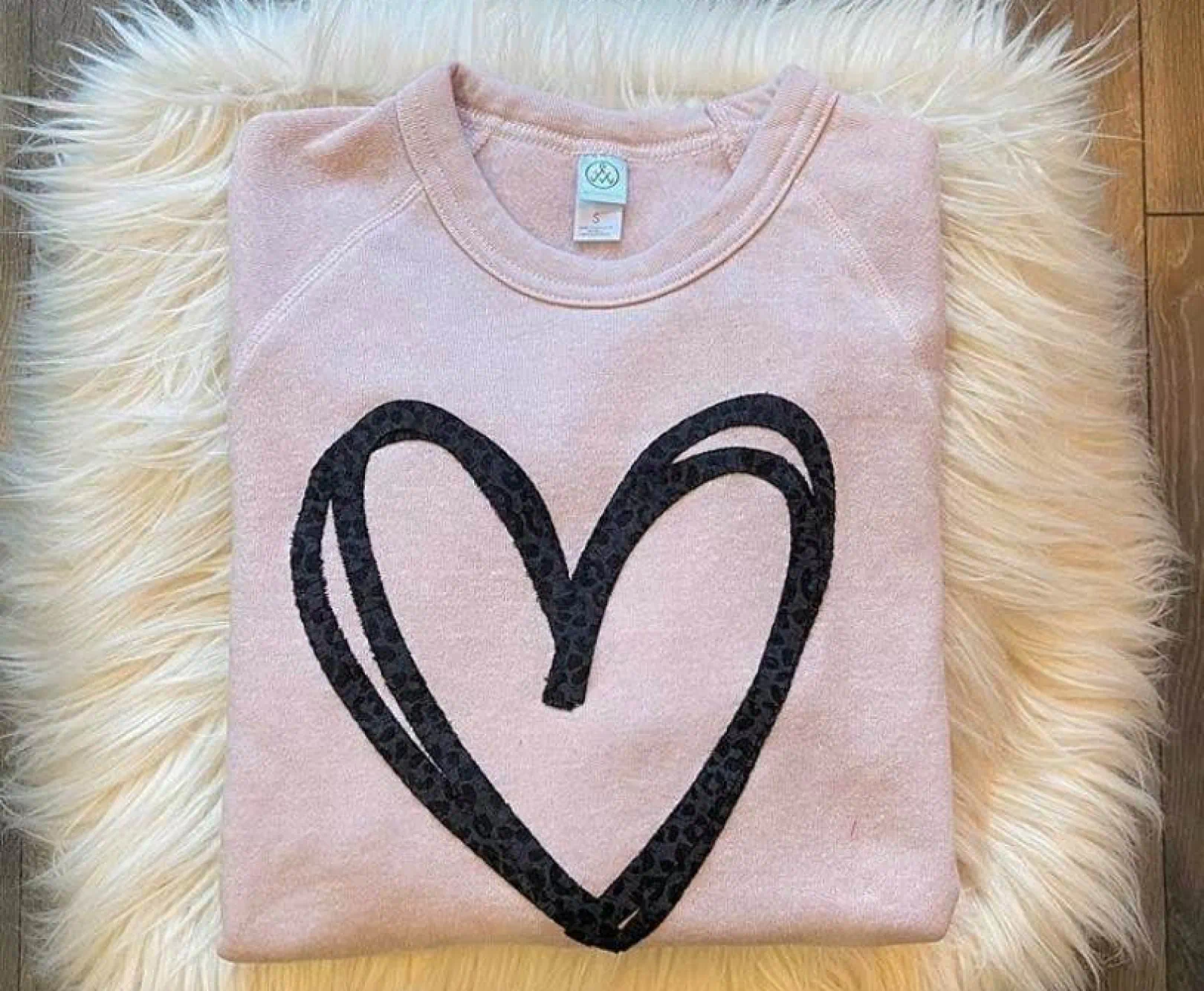 Folded pink sweatshirt with a black heart design on a fluffy white surface.