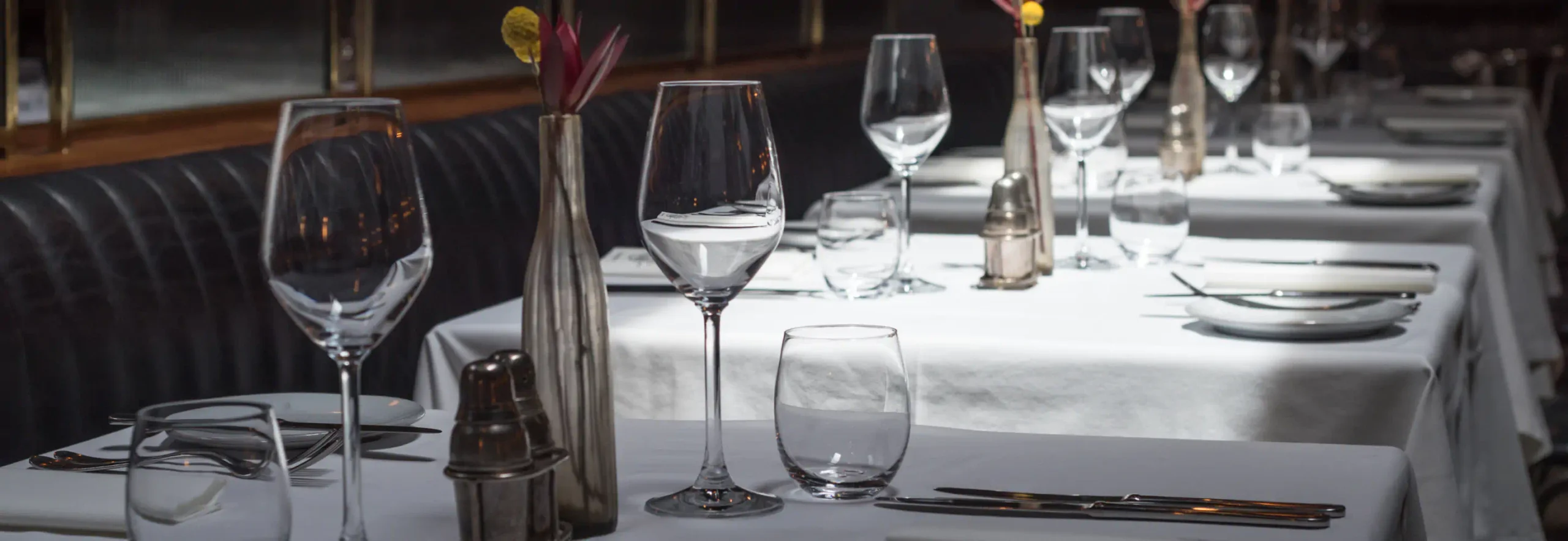 A row of tables in a nice restaurant set with wine glasses, white table cloths, and silver ware.