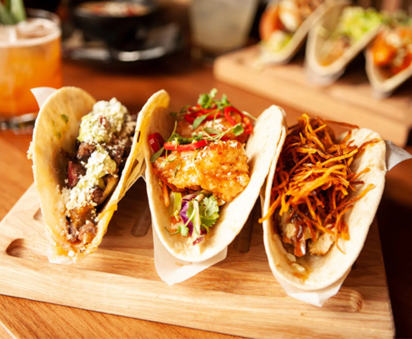 Three fish tacos sit on a wooden platter.